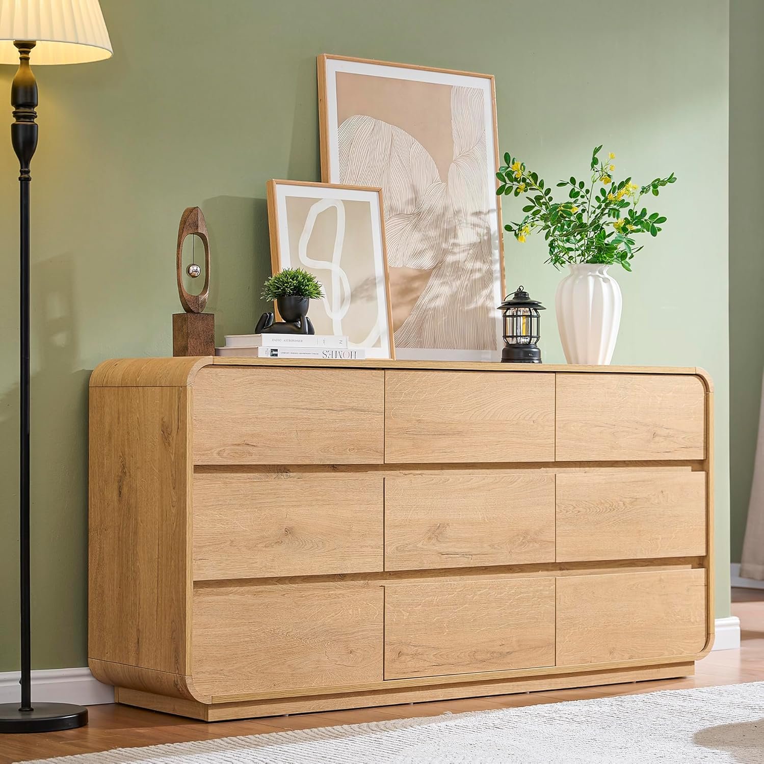 Standifurno 9-drawer wide curved oak dresser styled with framed art and greenery in a sage green bedroom